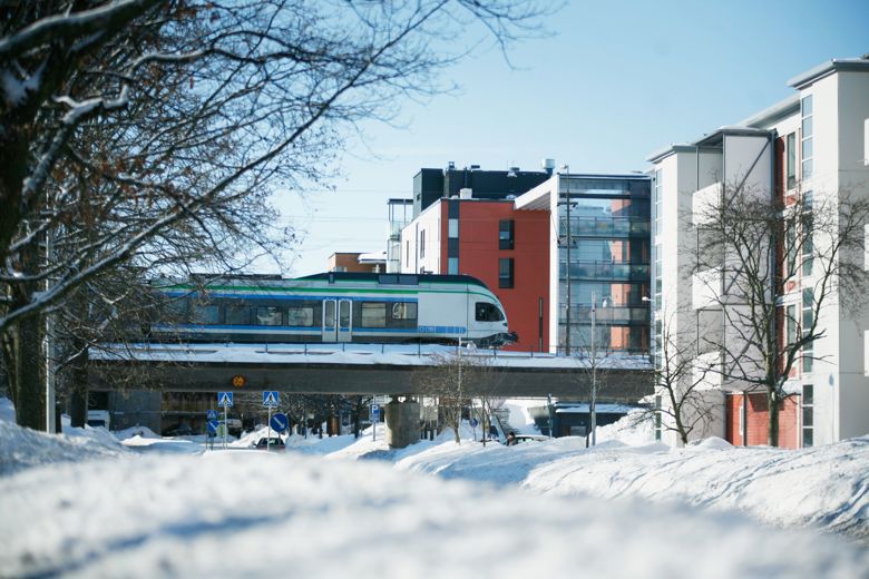 Juna kulkee sillalla talojen väliin lumisessa maisemassa.