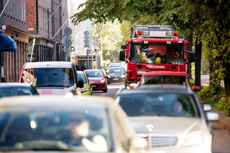 Vilkasliikenteinen katu, jossa paljon autoja. Kadun vasemmalla reunalla rakennuksia ja oikealla puita.