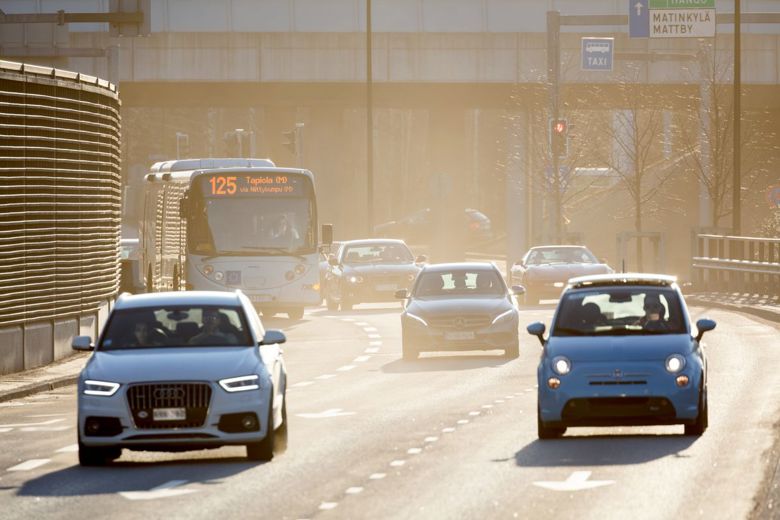 A photo of the road, with passenger cars and buses. The visibility is hampered by street dust in the air.