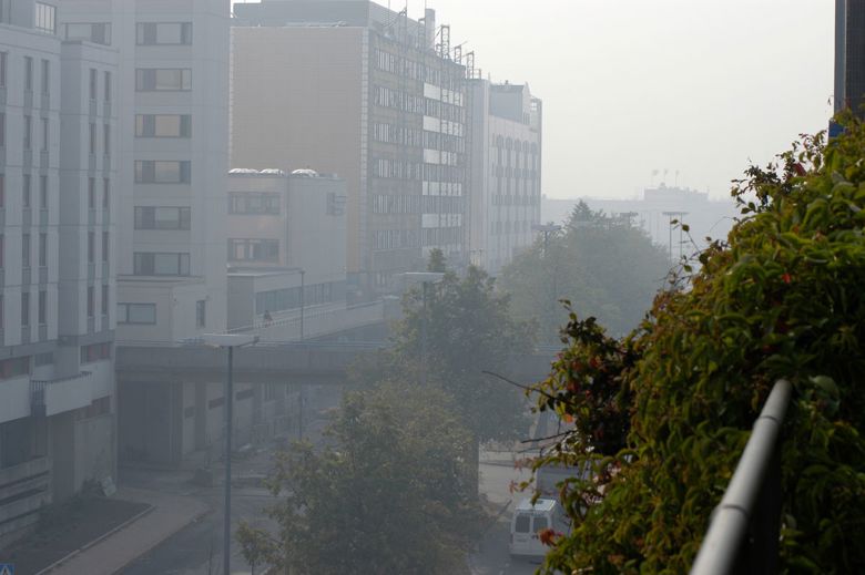 The fine particles from long-range transport reduce visibility, and the buildings, street, cars and vegetation are foggy when the distance even slightly increases. The image is sharp in the foreground.  